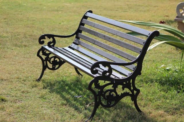 An artistic wrought iron park bench set on lush green grass under bright sunlight.
